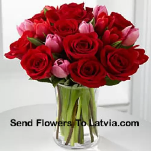 11 roses rouges et 6 tulipes roses avec quelques garnitures saisonnières dans un vase en verre